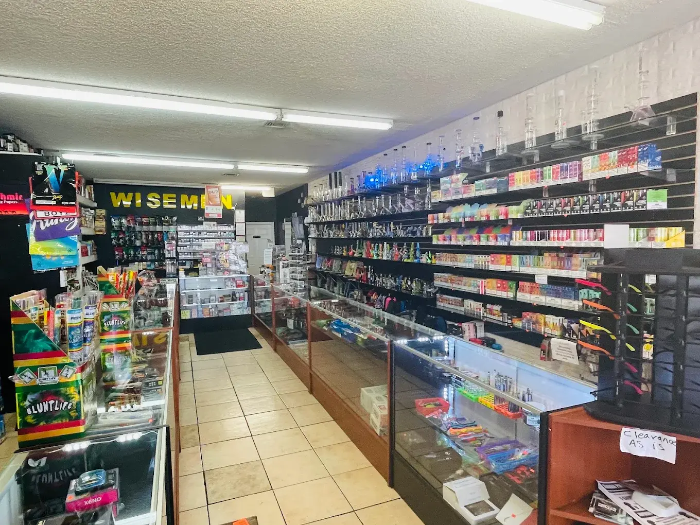 Wide interior aisle of Smoke N' Stuff lined with product shelving under the Wisemen sign.